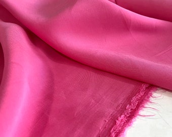Puede incluir: Primer plano de una tela de color rosa brillante con una superficie ligeramente texturizada. La tela está doblada y los bordes están deshilachados.