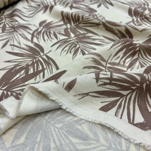 Peut inclure: Gros plan sur un tissu blanc avec un imprimé de feuilles tropicales brunes. Le tissu est plié et les bords sont visibles.