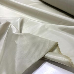 May include: Off-white fabric with a silky sheen. The fabric is draped, showing folds and texture. The material appears to be lightweight and flowing, with a subtle luster. The fabric is likely used for apparel or home decor.