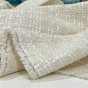 May include: Close-up of a white woven fabric with a textured surface. The fabric has a subtle sheen and a slightly frayed edge.