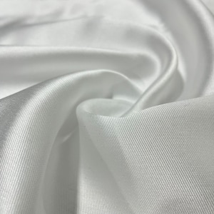 Könnte beinhalten: Weißer Satinstoff mit einer dezenten Rippenstruktur. Der Stoff ist glatt und seidig, mit einem leichten Glanz.