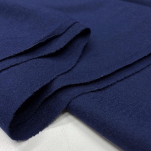 May include: Close-up of a folded piece of navy blue fabric. The fabric has a soft, textured appearance with visible folds and edges. The deep blue color is consistent throughout the material, suggesting a solid dye.