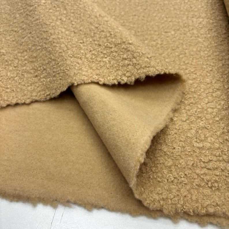 May include: A close-up of a beige fabric with a textured, fuzzy surface. The fabric is folded over to show the smooth, plain side.