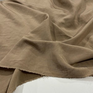 Puede incluir: Primer plano de una tela marrón con un brillo sutil. La tela está doblada y tiene un borde sin rematar.