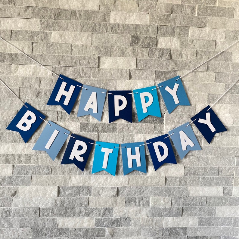 May include: A blue and white banner with the words "Happy Birthday" in white letters. The banner is made of paper and has a scalloped edge.