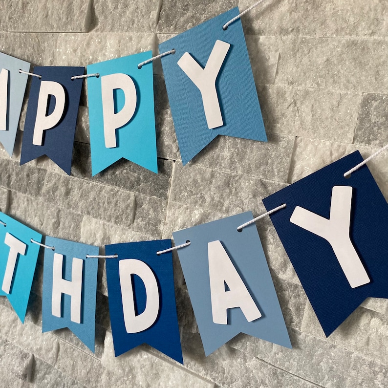 May include: A blue and white banner with the words "Happy Birthday" in white letters. The banner is made of paper and has a scalloped edge.