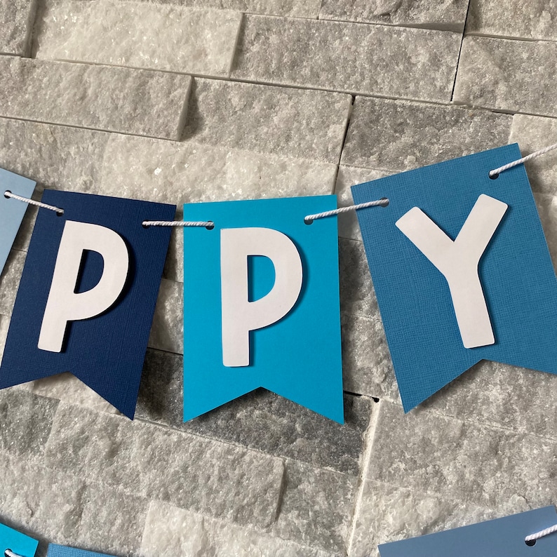 May include: A blue and white banner with the word "HAPPY" spelled out in white letters. The banner is made of felt and has a string running through it.