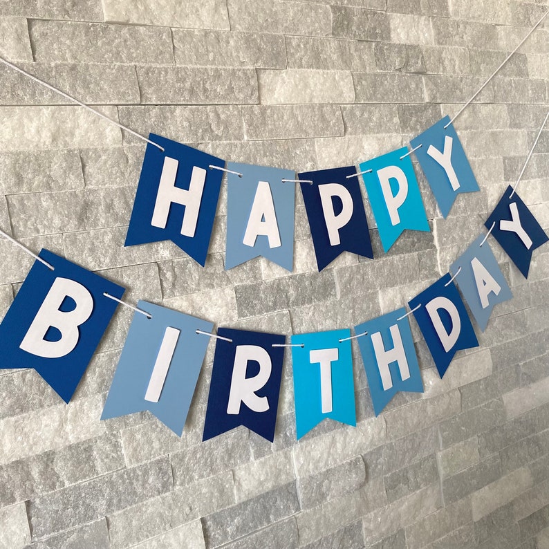 May include: A blue and white banner with the words "Happy Birthday" in white letters. The banner is made of felt and has a scalloped edge.