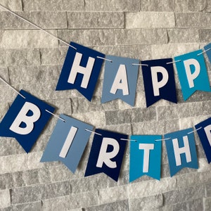 May include: A blue and white banner with the words "Happy Birthday" in white letters. The banner is made of paper and has a scalloped edge.