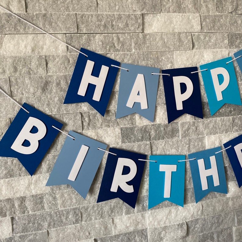 May include: A blue and white banner with the words "Happy Birthday" in white letters. The banner is made of paper and has a scalloped edge.