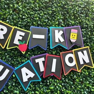 K&ouml;nnte beinhalten: Ein farbenfrohes Banner mit den Worten "Pre-K Graduation" in wei&szlig;en Buchstaben auf schwarzem Filz. Jeder Buchstabe befindet sich auf einem separaten Wimpel mit einem andersfarbigen Rand. Die Wimpel sind mit einem roten Apfel, einem gelben Bleistift mit einem Smiley und einem schwarzen Strich verziert.