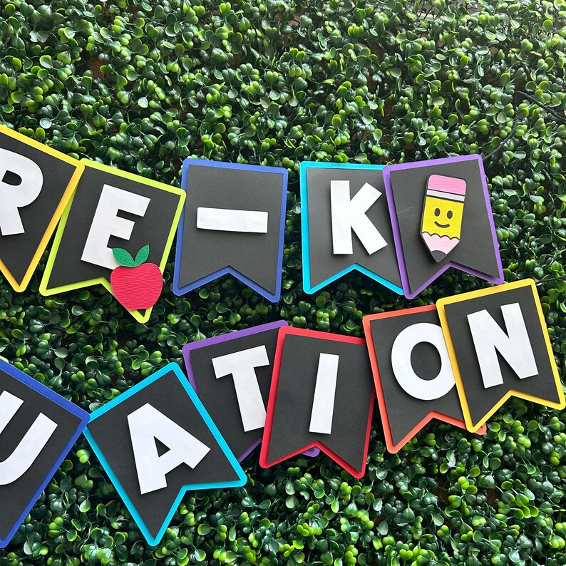 K&ouml;nnte beinhalten: Ein farbenfrohes Banner mit den Worten "Pre-K Graduation" in wei&szlig;en Buchstaben auf schwarzem Filz. Jeder Buchstabe befindet sich auf einem separaten Wimpel mit einem andersfarbigen Rand. Die Wimpel sind mit einem roten Apfel, einem gelben Bleistift mit einem Smiley und einem schwarzen Strich verziert.