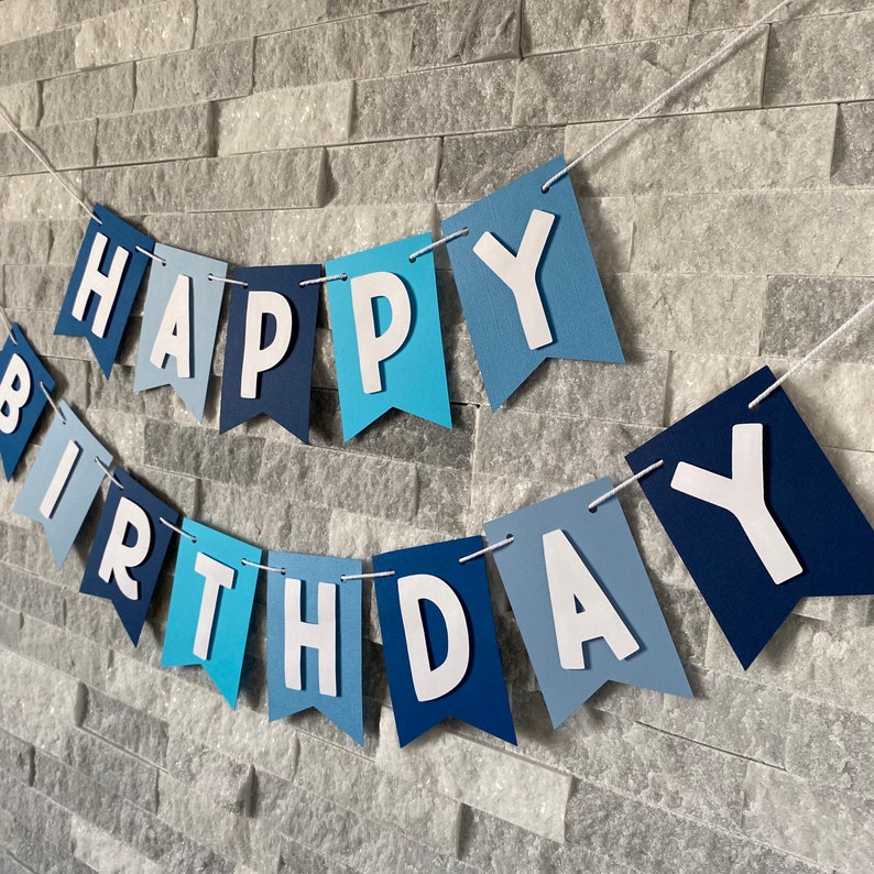 May include: A blue and white "Happy Birthday" banner with pennants in shades of blue. The letters are white and the banner is strung with white thread.