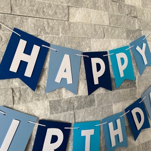 May include: A blue and white banner with the words "Happy Birthday" in white letters. The banner is made of paper and has a scalloped edge.