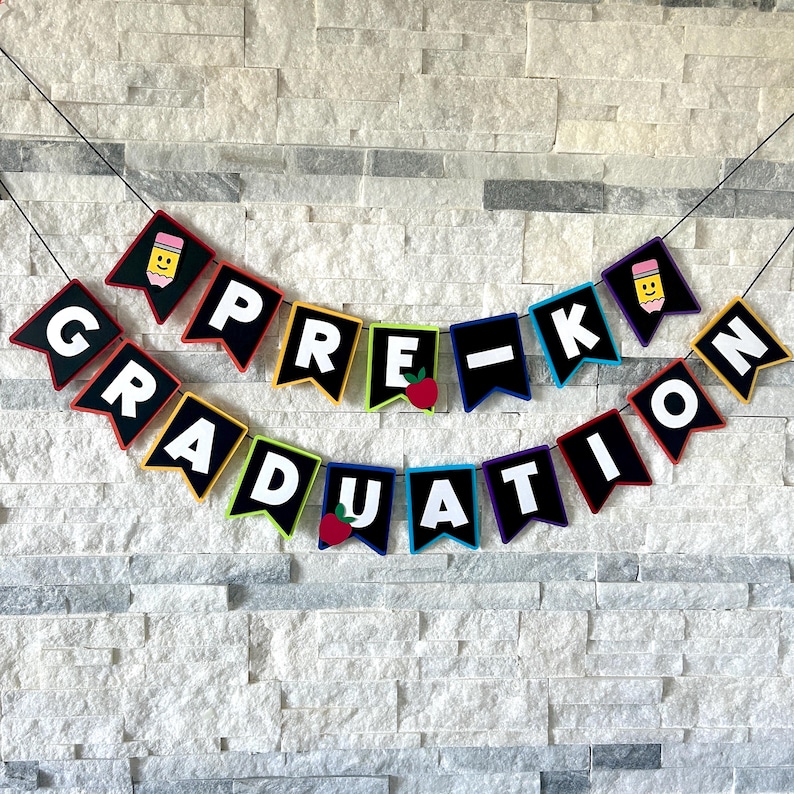 K&ouml;nnte beinhalten: Ein farbenfrohes Banner mit schwarzen Filzbuchstaben, auf dem "Pre-K Graduation" steht. Die Buchstaben sind in verschiedenen Farben umrandet und haben kleine Illustrationen von Bleistiften und &Auml;pfeln.
