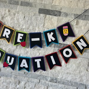 K&ouml;nnte beinhalten: Ein farbenfrohes Banner mit den Worten "Pre-K Graduation" in wei&szlig;en Buchstaben auf schwarzen Flaggen. Jede Flagge hat einen andersfarbigen Rand und eine kleine Dekoration, darunter ein Apfel und ein Bleistift.