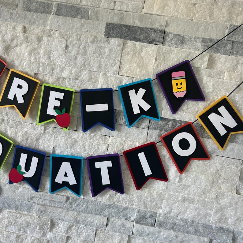 K&ouml;nnte beinhalten: Ein farbenfrohes Banner mit den Worten "Pre-K Graduation" in wei&szlig;en Buchstaben auf schwarzen Flaggen. Jede Flagge hat einen andersfarbigen Rand und eine kleine Dekoration, darunter ein Apfel und ein Bleistift.