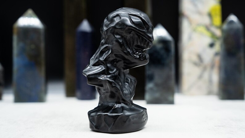 May include: A black sculpture of a creature with a detailed, textured surface. The sculpture has a menacing expression with visible teeth and a defined jawline. Various crystal obelisks are in the background.