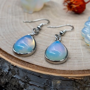 May include: A pair of silver teardrop earrings with iridescent opal stones. The earrings have a simple design and are perfect for everyday wear.