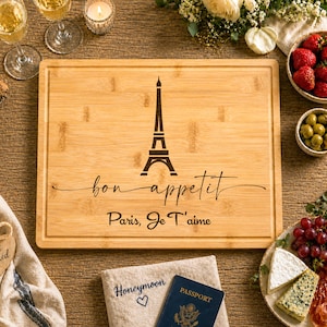 May include: A rectangular bamboo cutting board featuring a laser-engraved illustration of the Eiffel Tower. Below the tower, the text reads "bon appetit" in a cursive script, followed by the printed text "Paris, Je T'aime" in a simple font.