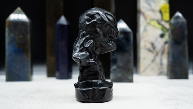 May include: A black sculpture of a creature's head with a detailed, textured surface. The sculpture is set against a backdrop of various crystal obelisks in shades of blue, green, and gray.