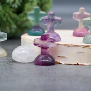 May include: A collection of small, colorful, crystal crosses. The crosses are made of fluorite and are in shades of purple, green, and white. The crosses are arranged on a wooden surface.