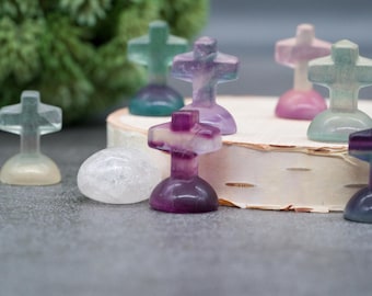 May include: A collection of small, colorful, crystal crosses. The crosses are made of fluorite and are in shades of purple, green, and white. The crosses are arranged on a wooden surface.