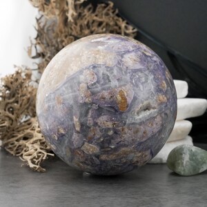May include: A large, spherical decorative object with a marbled appearance. The sphere features a mix of purple, tan, and brown hues, with a polished surface. The object is likely a decorative stone or crystal, suitable for home decor.