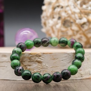 Puede incluir: Un brazalete de piedras preciosas verdes y rosas con cuentas redondas. El brazalete está hecho de piedras naturales y es una hermosa joya.
