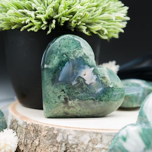 May include: A collection of green moss agate heart shaped stones. The stones are polished and have a natural, organic look.