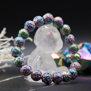 Peut inclure: Un bracelet de perles aux couleurs irisées, composé de perles texturées violettes, bleues et vertes. Chaque perle mesure environ 2 cm de diamètre. Le bracelet est présenté sur un fond sombre, mettant en valeur ses couleurs.
