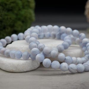 May include: Two blue lace agate beaded bracelets stacked on top of each other. The beads are round and have a light blue color with white swirls.