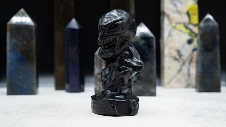 May include: A black sculpture of a creature with a detailed face and body, set against a backdrop of various crystal obelisks. The sculpture is the focal point, with the obelisks adding depth.