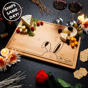 May include: A personalized bamboo cutting board with a bunny rabbit design and the text "The Grokes" engraved on the bottom right corner. The board is filled with cheese, crackers, fruit, and other snacks.