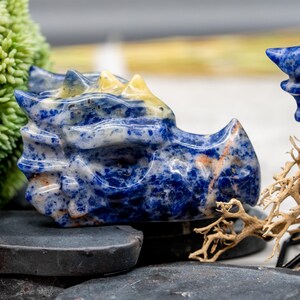 May include: A blue and yellow dragon head carved from a single piece of sodalite. The dragon head is a decorative object with a smooth, polished finish.