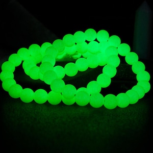 May include: A set of three glow-in-the-dark bracelets made of green beads. The bracelets are stacked on top of each other.