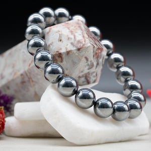 May include: A silver hematite beaded bracelet with a high polish finish. The bracelet is displayed on a white stone surface.