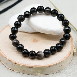 May include: A black gemstone bracelet with round beads. The bracelet is on a wooden surface.