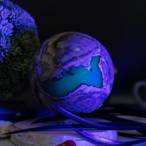 Peut inclure: Un objet décoratif sphérique avec un extérieur violet et gris et un intérieur turquoise. L'objet est éclairé par une lumière bleue, créant un contraste saisissant. Le thème général est artistique et décoratif.