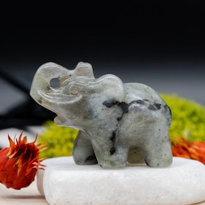 May include: A small, carved elephant figurine made of green labradorite stone. The elephant has a raised trunk and black veins throughout the stone.