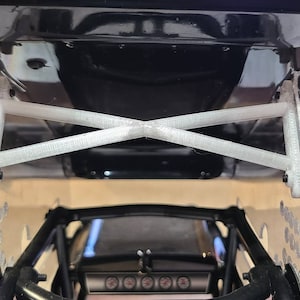 May include: A white 3D printed chassis brace for a remote control car. The brace is designed to add strength and rigidity to the chassis.
