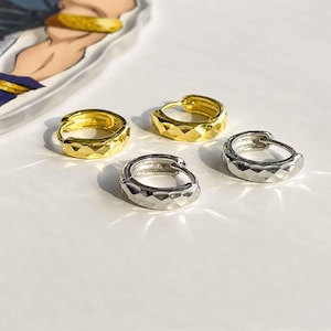May include: Two pairs of small hoop earrings, one pair in a polished gold tone and one pair in a polished silver tone. Each hoop features a faceted, geometric surface texture that reflects light, creating a series of small, angular planes.