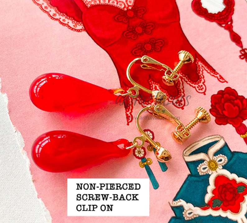 Pu&ograve; includere: Orecchini rossi a goccia con chiusura a clip e elementi dorati. Gli orecchini hanno una clip a vite e piccoli nappe decorative. Lo sfondo presenta illustrazioni di abiti tradizionali cinesi e motivi floreali.
