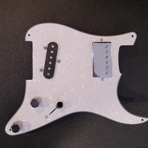 May include: White electric guitar body with a white pearl finish. The body has two black pickup covers, a chrome bridge pickup cover, and three knobs.