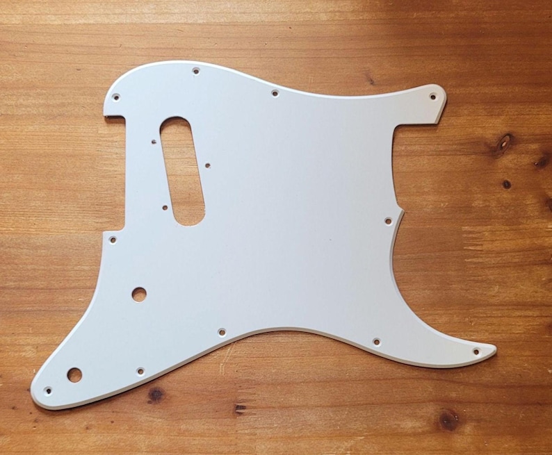 Op de afbeelding: Een witte gitaar slagplaat met een gebogen vorm en meerdere schroefgaten. De slagplaat heeft een langwerpige ovale uitsparing voor de pickup en is ontworpen om op een specifiek gitaarmodel te passen. Het oppervlak is glad en de kleur is effen wit.