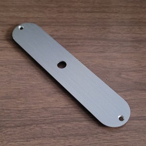 May include: A brushed silver metal guitar control plate with two screw holes and a single hole in the centre.