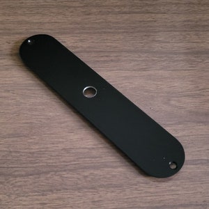 May include: Black metal guitar pickguard with a single round hole in the centre.