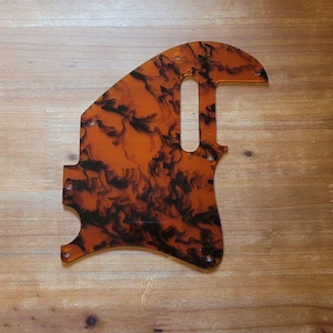 Op de afbeelding: Een gitaar slagplaat met een schildpadpatroon. De slagplaat heeft een warme oranje kleur met zwarte marmering. Het heeft verschillende schroefgaten en een uitsparing voor de pickup. De slagplaat is gemaakt van duurzaam materiaal en beschermt de gitaar.