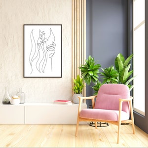 Peut inclure: Une impression encadrée noire d'un dessin au trait de deux visages, l'un avec de longs cheveux, accrochée à un mur blanc au-dessus d'une armoire blanche. Un fauteuil rose est placé devant une fenêtre avec des plantes vertes.