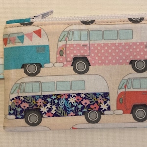 May include: A white zippered pouch with a colorful print of vintage camper vans. The pouch has a key chain attached.